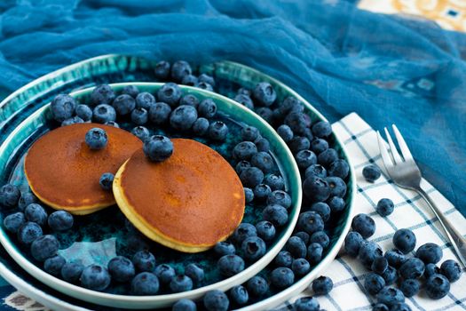 selective focus. pancakes with blueberries on a blue plate. Lots of fresh blueberries scattered around. Delicious dessert with berries for breakfast. High quality photo