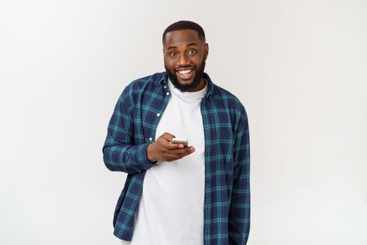 Smiling African American young man holding phone looking at smartphone isolated on white grey studio background