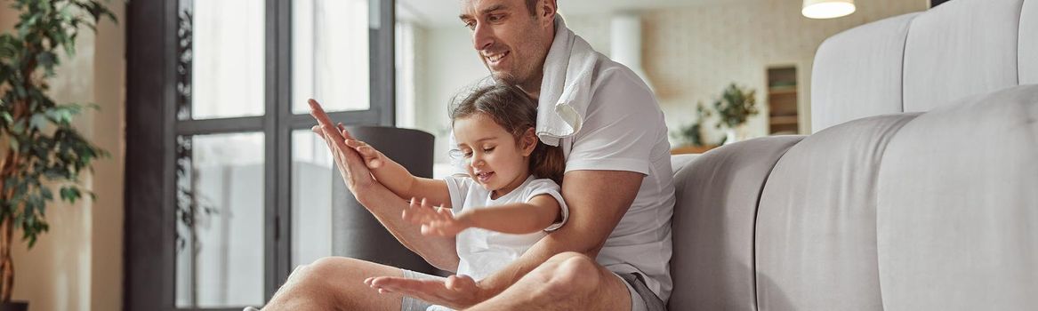 Low angle of smiling man with little girl sitting on floor in living room and having fun