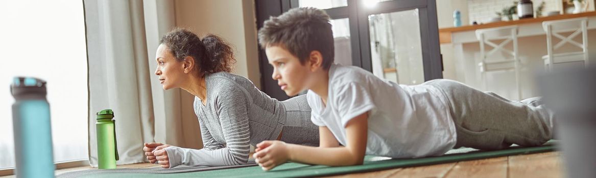 Low angle of slim woman and strong boy staying in plank position during powerful workout