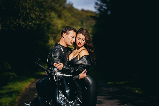 Handsome young man and beautiful young girl, couple sitting on a motorcycle, standing near a motorcycle in black leather clothes, hugging, in nature, on the street