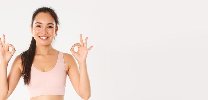 Sport, wellbeing and active lifestyle concept. Close-up of smiling, satisfied asian sportswoman recommend gym or yoga classes, showing okay gesture, pleased with perfect online coach.