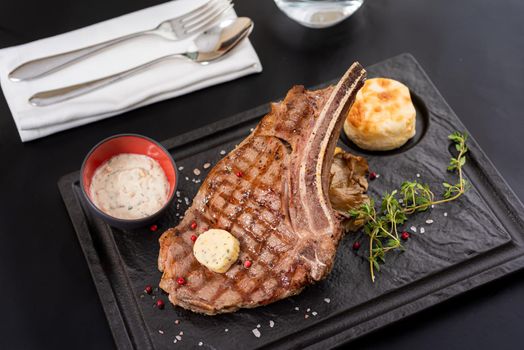 Grilled veal cutlet on black stone plate with sauce and garnish.