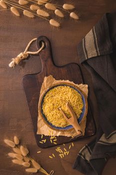 Dry risoni pasta in a ceramic bowl on a rustic kitchen countertop.