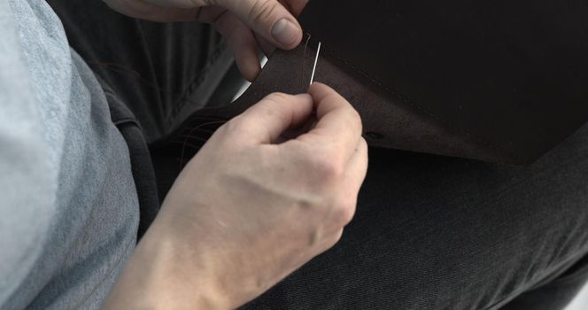 Craftsman sewing a handmade brown leather wallet in workshop