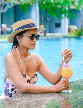 Asian women with a hat relaxing in the swimming pool with a cocktail in hand, women swimming pool banner holiday vacation concept, Asian women in blue swimming pool luxury vacation