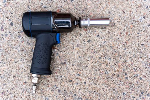 a pneumatic impact wrench with an end head lies on the concrete floor. Car repair, workshop.