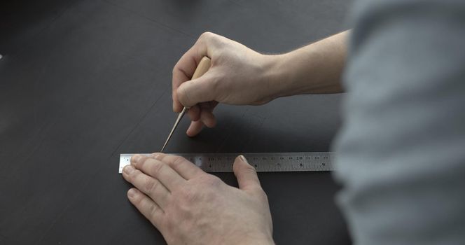 Close up of leather craftsman working with natural leather by awl and ruler. Handmade master at work in local workshop. Leather wallet stitch