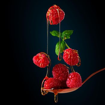 Falling raspberries. food levitation on dark background. ripe raspberries and honey