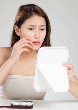 Portrait of young ardent asian woman looking in the mirror worry about pimple on her face. Beauty care for skin problem, acne treatment concept.