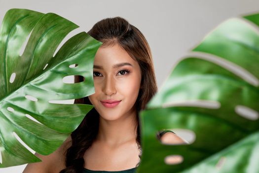 Closeup portrait of young ardent woman with healthy fair skin holding big green leaf near her face. Skin care beauty care concept.