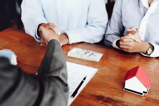 Real estate agents shake hands with customers after signing documents.