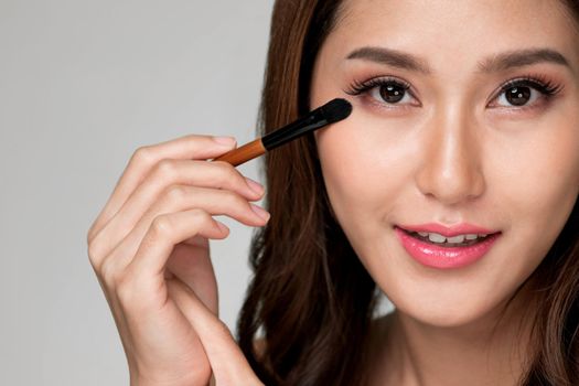 Closeup ardent young woman with healthy fair skin applying her eyeshadow with brush. Female model with fashion makeup. Beauty and makeup concept.