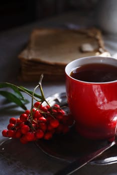 Red cup of tea on vintage metal plate with a bunch of red rowan, autumn morning tea concept, selective focus.