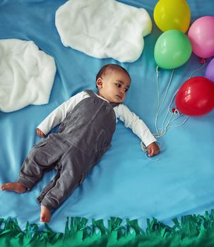 Up, up and away. Concept shot of an adorable baby boy flying through the sky holding a bunch of balloons