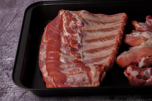 raw pork ribs on a black tray ready for oven roasting