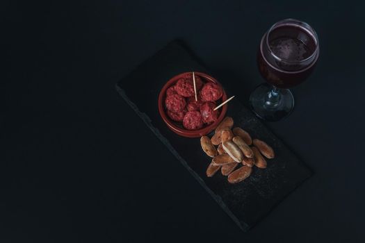 close-up of a tapa of chorizo in sauce, typical Spanish sausage with bread and summer red wine isolated on black background