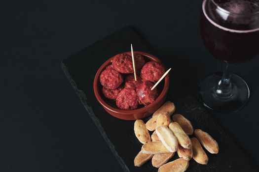 close-up of a tapa of chorizo in sauce, typical Spanish sausage with bread and summer red wine isolated on black background