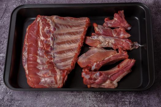 raw pork ribs on a black tray ready for oven roasting