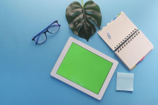 top view of digital tablet with office suppliers on blue background .