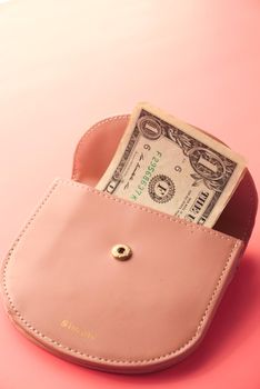 Us dollar cash in a small wallet on pink background .