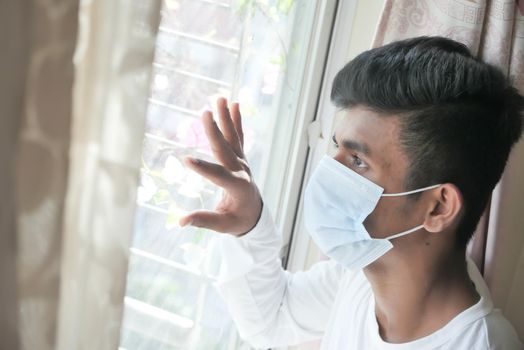 A young man with protective mask looking through window .