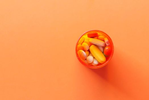 top view of pills and capsule in a container on orange background .