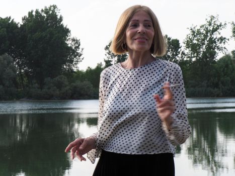 female pensioner having fun and smoking a cigarette in a park - aging free and wellness concept