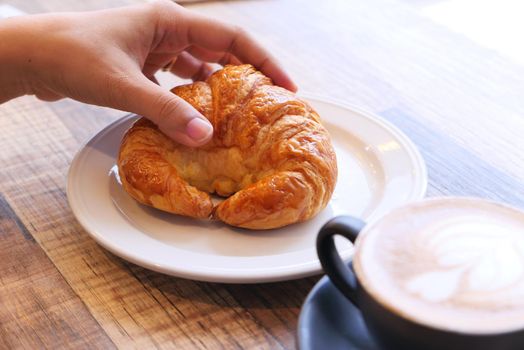 women hand holding croissant on wooden table.