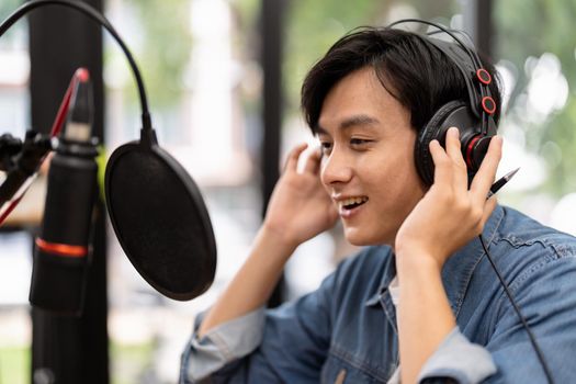Asian male podcaster making audio podcast from her home studio.