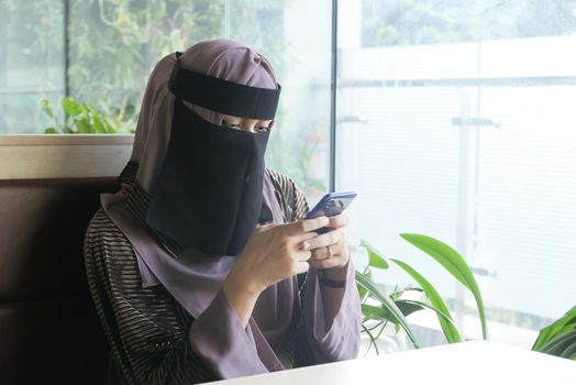 Muslim women with head scarf using smart phone indoor .