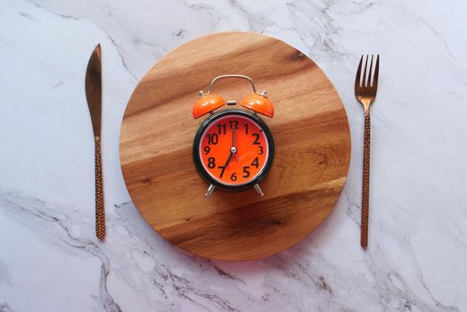 Alarm clock on plate on wooden table, top view