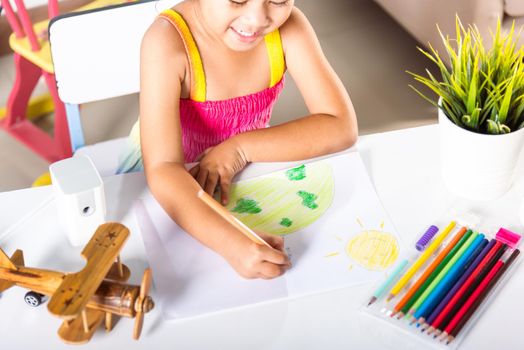 Happy child little girl colorful drawing family standing hold hands on planet earth on paper, Asian cute kid preschooler sit on table smiling she draw picture with pencil at home, earth day concept