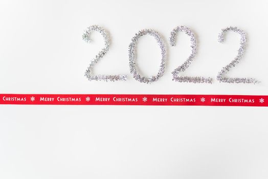 Happy new year 2022 written with foil and new year rain on an isolated white background along with a ribbon with the inscription merry christmas