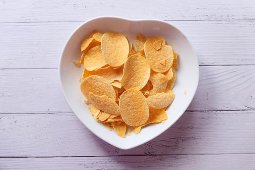 Bowl with tasty potato chips on wooden background