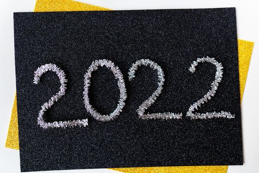 The year 2022 is written in New Year's silver tinsel on a black background. Greeting card