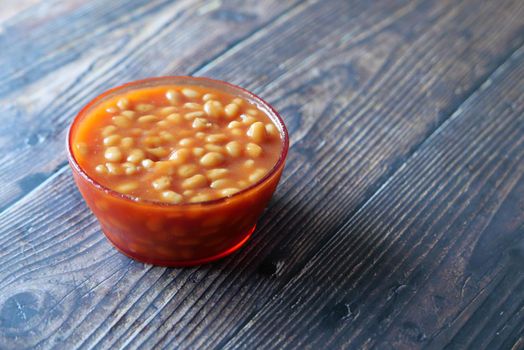 Tasty baked beans in a bowl on wooden background