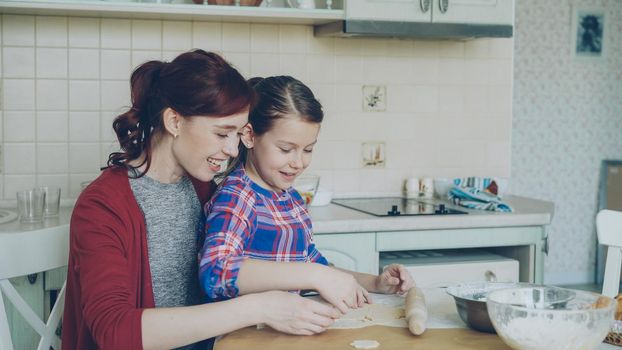 Smiling mother and cute daughter making Christmas cookies together sitting at modern kitchen at home. Family, food and people concept