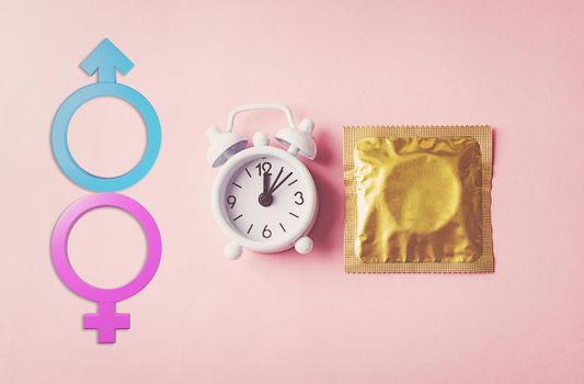 World sexual health or Aids day, condom in wrapper pack and Alarm clock birth control and Male and female gender signs, studio shot isolated on a pink background, activism and relationship sex concept