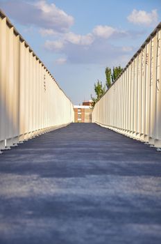 Textured abstract pattern with sunset shadows on an empty pedestrian walkway bridge in Madrid.Clouds and blue sky. Facade with windows in the end background. Light at the end. Diminishing perspective