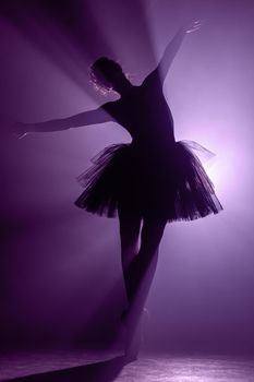 Ballet dancer in tutu performing, dancing on stage. Ballerina practices on floor in dark studio with smoke. Neon light. High quality photo