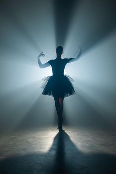 Ballet dancer in tutu performing, dancing on stage. Ballerina practices on floor in dark studio with smoke. Neon light. High quality photo