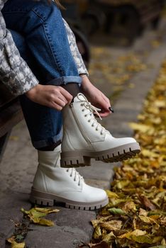 Female legs in a jeans and white fashion boots with laces. fallen leaves on the sidewalk