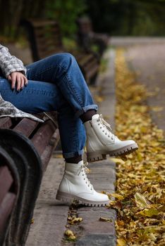 Female legs in a jeans and white fashion boots with laces. fallen leaves on the sidewalk