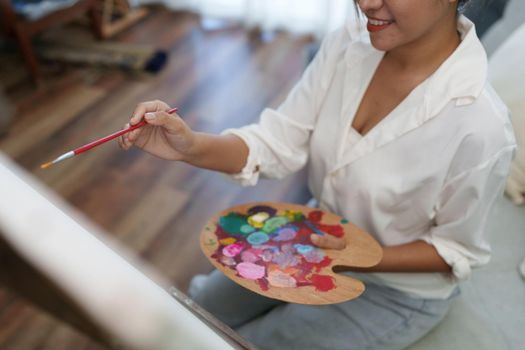 Joyful young female artist painting on canvas at workshop.