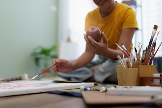 Joyful young female artist painting on canvas at workshop.