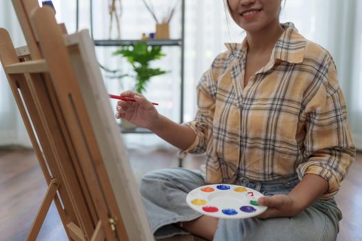 Joyful young female artist painting on canvas at workshop.