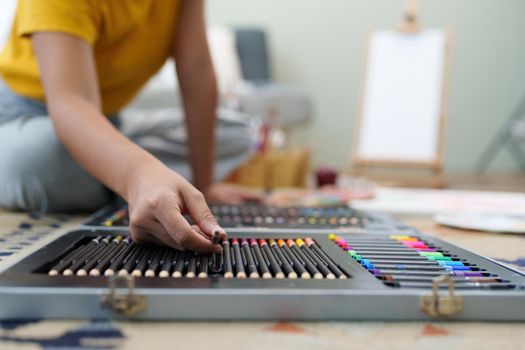 Joyful young female artist choosing colour pencil at workshop.