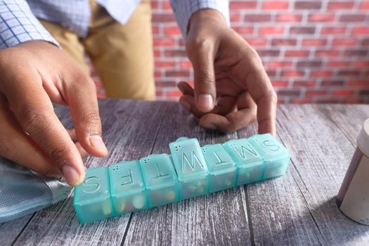 man's hands taking medicine from a pill box .