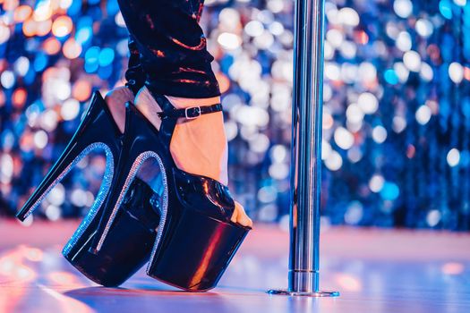 Legs in high sexy shoes near pylone. Striptease dancer moving on stage in strip night club. Pole dancing background. High quality photo